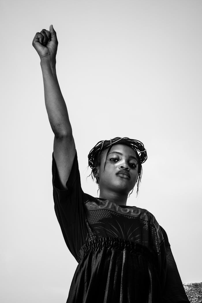 Black and white portrait of a woman raising her fist, symbolizing empowerment and strength.